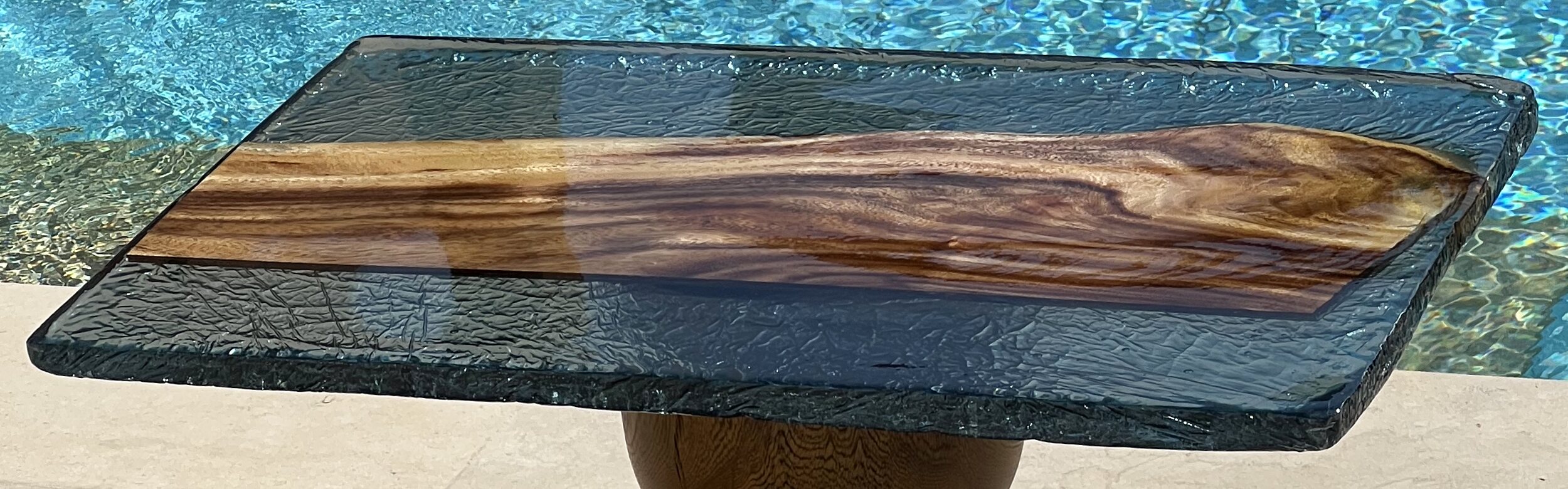 The Strata slab read close — raw crackled cast edge, rippled smoke-turquoise resin, and the figured wood spine running through the pour